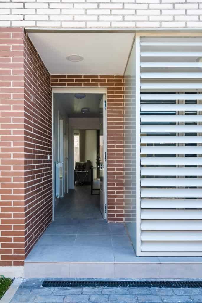 Stylish entrance with brick walls, modern louvered panels, and clean design for home exterior.